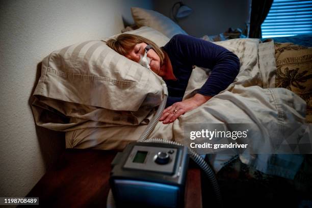 middle aged woman in her fifties sleeping peacefully in her bed using a cpap machine to provide therapy for sleep apnea - sleep apnea stock pictures, royalty-free photos & images