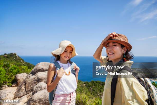 two japanese women wearing hats standing on a cliff, ocean in the background. - アウトドア　日本人 ストックフォトと画像