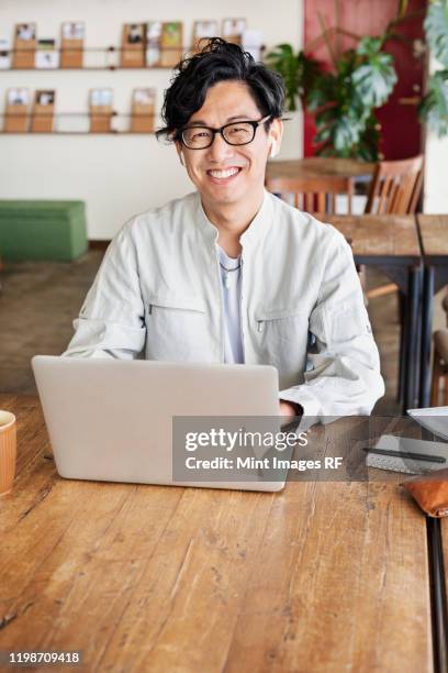 male japanese professional sitting at a table in a co-working space, using laptop computer. - creative rf stock pictures, royalty-free photos & images