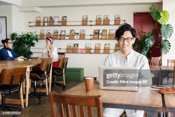 group of young japanese professionals working on laptop computers in a co-working space. - creative rf stock pictures, royalty-free photos & images