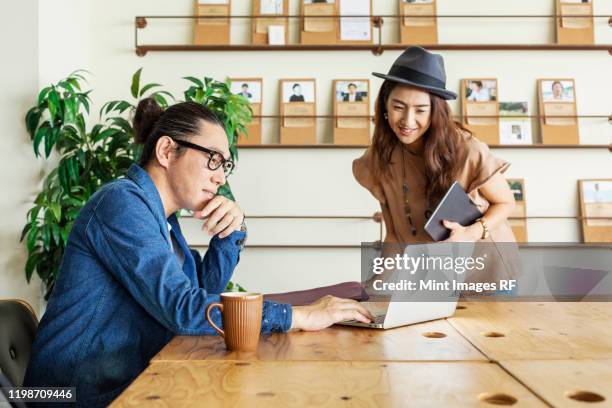 male and female japanese professional at a table in a co-working space, using laptop computer. - creative rf stock pictures, royalty-free photos & images