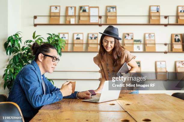 male and female japanese professional at a table in a co-working space, using laptop computer. - rf business stock-fotos und bilder