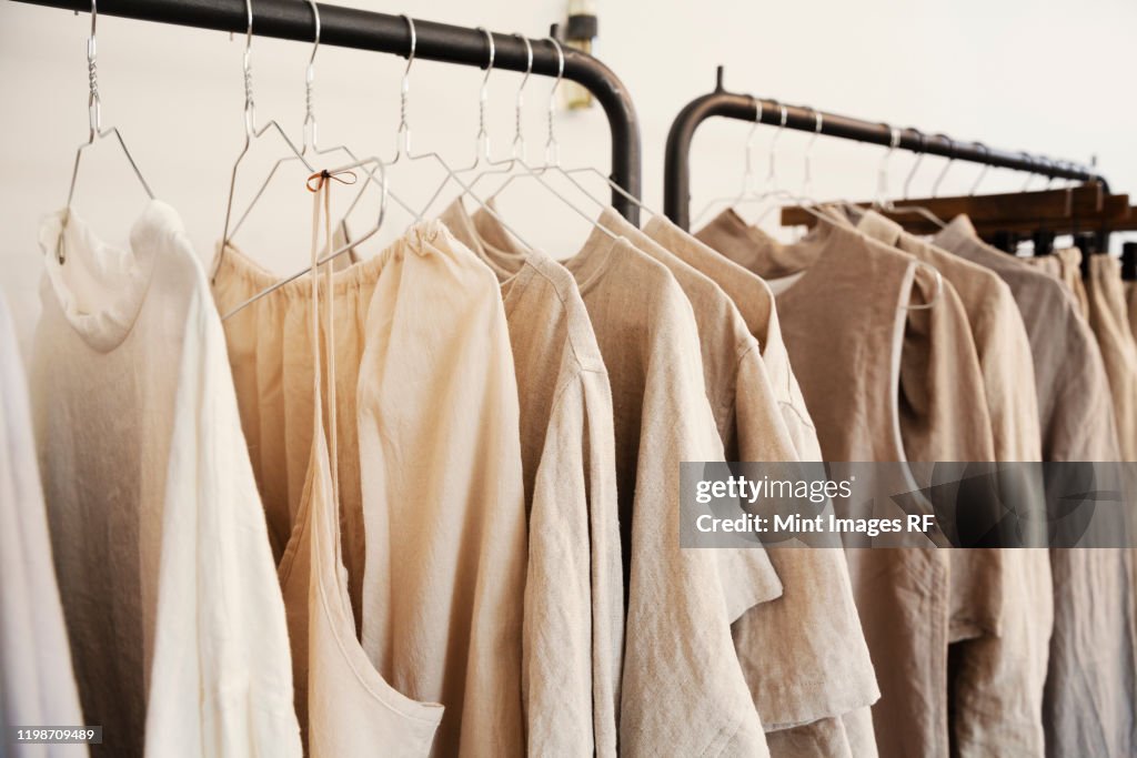 Close up of a selection of clothes in natural colours on a rail in a boutique.