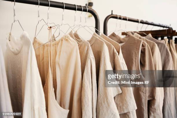 close up of a selection of clothes in natural colours on a rail in a boutique. - sustainable clothing stock pictures, royalty-free photos & images