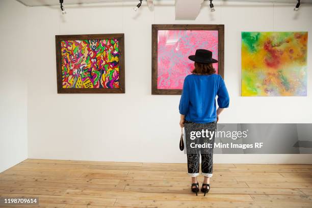 japanese woman wearing hat standing in front of abstract painting in an art gallery. - in museum stock pictures, royalty-free photos & images