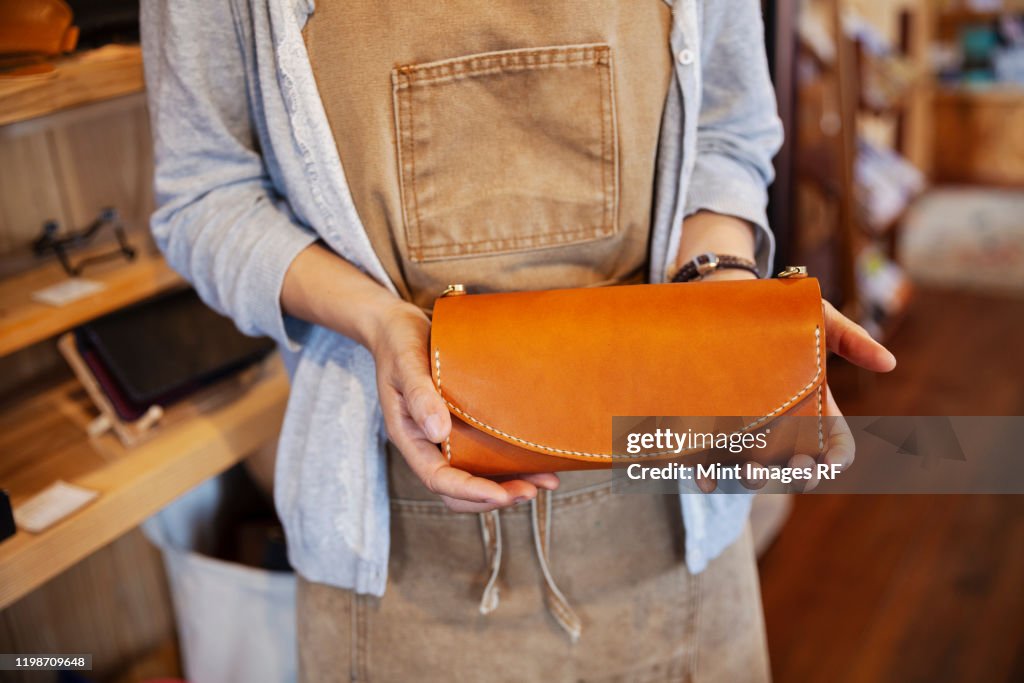 Close up of woman standing in a leather shop, holding tan leather clutch bag.