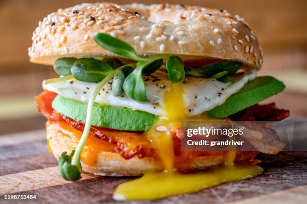 ontbijt bagel met ei, greens, avocado, spek, worst en kaas op een rustieke snijplank - roerei stockfoto's en -beelden
