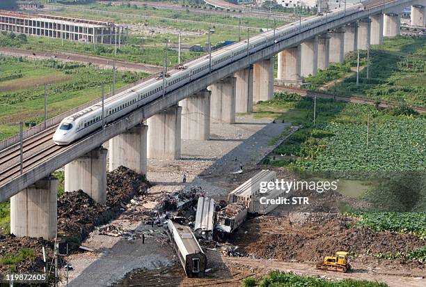 Bullet train passes the wreckage of two other high-speed trains which collided two days earlier, in the town of Shuangyu in the eastern Chinese...