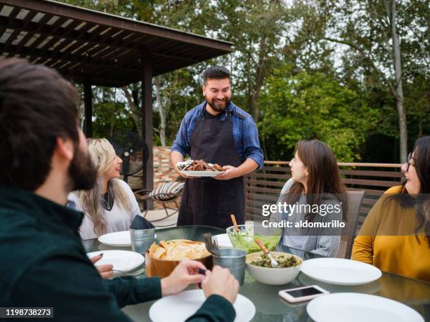 hombre latino llevando plato de comida a sus amigos - carne asada fotografías e imágenes de stock