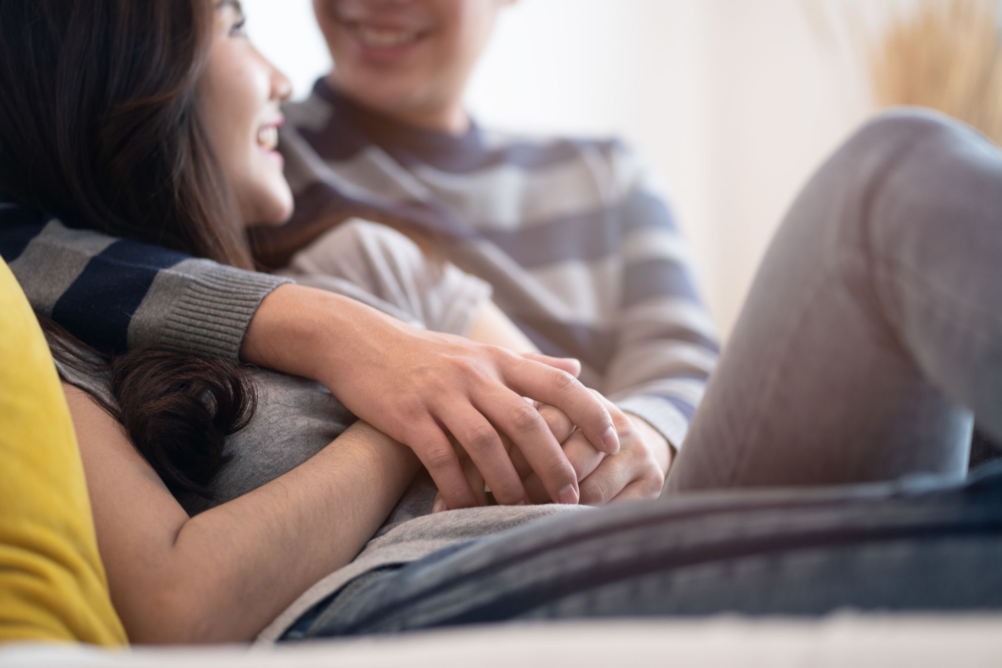 Lovely Asian couple sitting on bed in bedroom talking together with happiness. Boy hugging girl and holding hand, be hand in hand. Crop shot focus on hands. Man looking at woman eyes and smile face. Lovely Asian couple sitting on bed in bedroom talking together with happiness. Boy hugging girl and holding hand, be hand in hand. Crop shot focus on hands. Man looking at woman eyes and smile face.