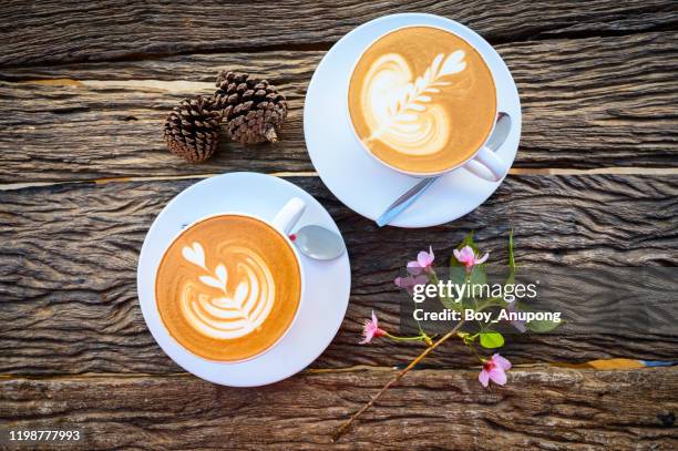 high angle view of a couple cup of hot latte coffee with small pine cones and sakura flowers on the wooden table. - kegelvrucht stockfoto's en -beelden