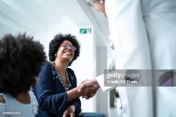 mujer médico senior dando la bienvenida / saludando a la madre y la hija en el hospital - clinica medica fotografías e imágenes de stock