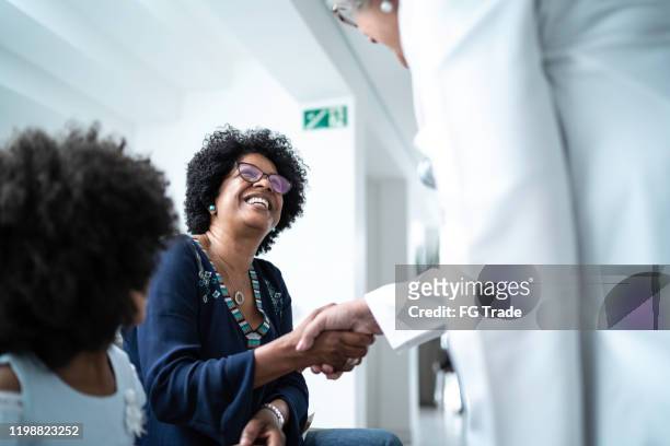 female senior doctor welcoming / greeting mother and daughter at hospital - visit stock pictures, royalty-free photos & images
