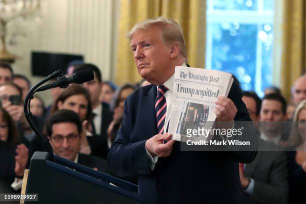 President Donald Trump holds up a newspaper as he speaks one day after the U.S. Senate acquitted on two articles of impeachment, in the East Room of...