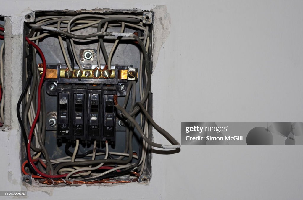 Dismantled fuse box and wiring under repair on the interior wall of a house