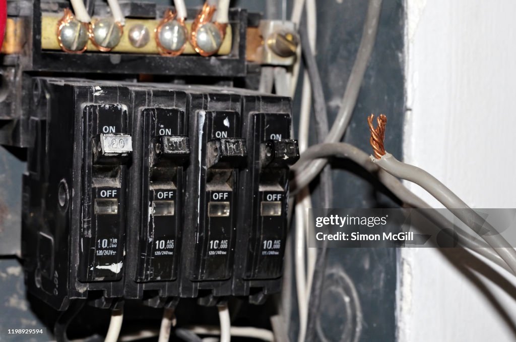 Dismantled fuse box and wiring under repair on the interior wall of a house