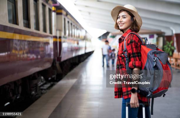 young asian woman traveler with backpack in the railway, backpack and hat at the train station with a traveler, travel concept. woman traveler tourist walking at train station - tourist fotografías e imágenes de stock