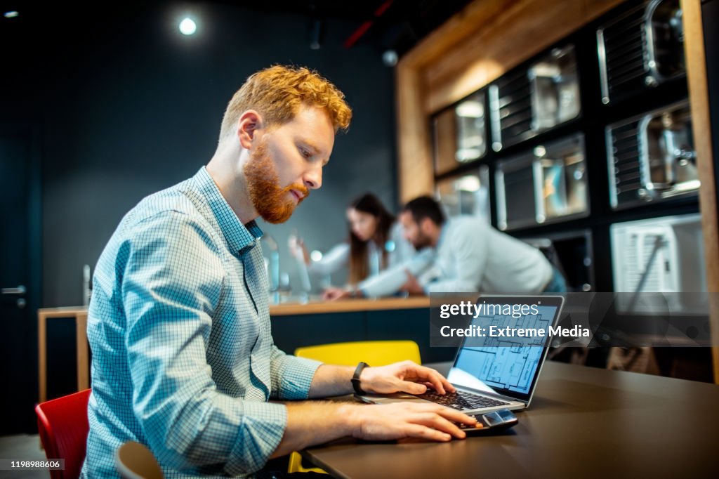 Een bebaarde man die wiskundige berekeningen maakt op een Home blauwdruk die hij heeft geopend op een laptop in een woning verbeterings winkel
