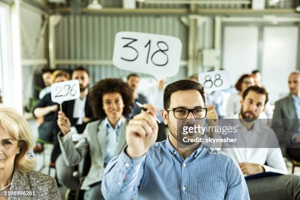crowd of business people having an auction in a board room. - auction stock pictures, royalty-free photos & images