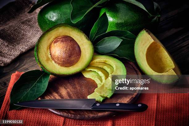 niedriger schlüssel nahaufnahme von grünen reifen avocados mit blättern - aguacates stock-fotos und bilder