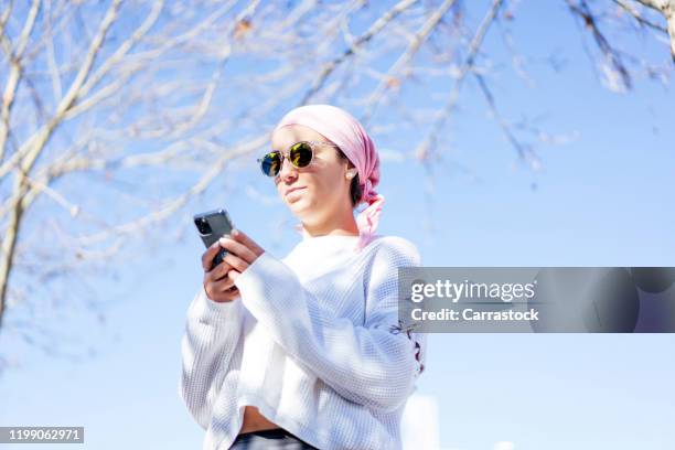 woman with cancer with pink scarf using mobile phone. - bandana - fotografias e filmes do acervo