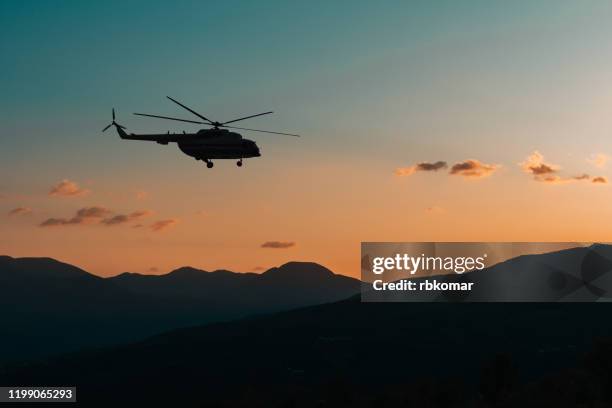 helicopter flies in the mountains at sunset in the dark - helikopter stockfoto's en -beelden