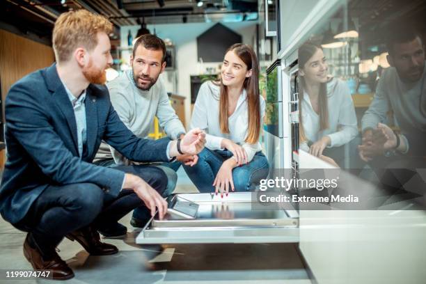 young husband and wife browsing for a dishwasher with a store seller assisting them in an upscale kitchen appliances and renovation shop - buying washing machine stock pictures, royalty-free photos & images