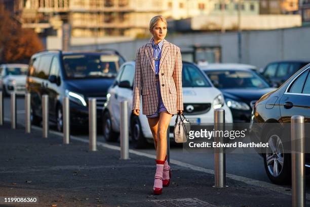 Caroline Daur wears a checked oversized blazer jacket, a Prada white and black bag, pink wool socks, red shoes, a blue striped shirt, outside Prada,...