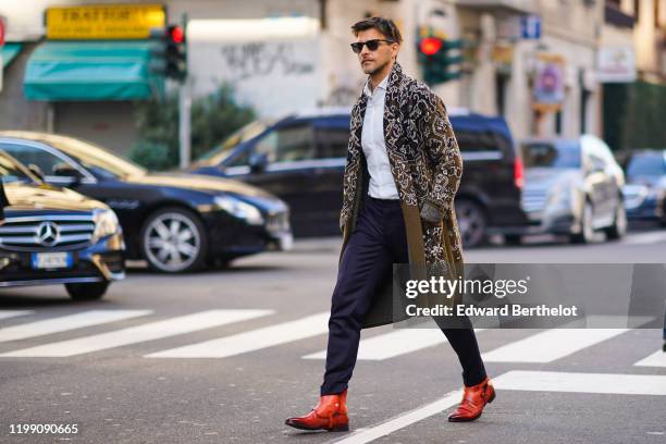 Johannes Huebl wears sunglasses, a shirt, dark blue pants, brown leather pointy shoes, a green khaki long wool jacket with printed geometric...