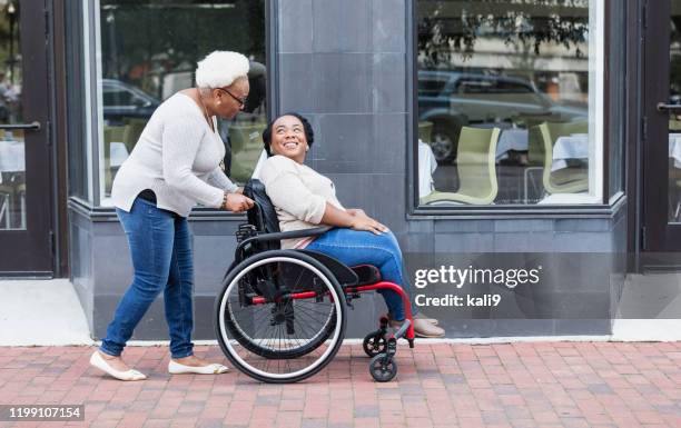 african-american woman in wheelchair with mother in city - of deformed people stock pictures, royalty-free photos & images