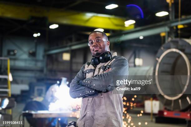 man in metal fabrication plant, welder in background - toughness man stock pictures, royalty-free photos & images