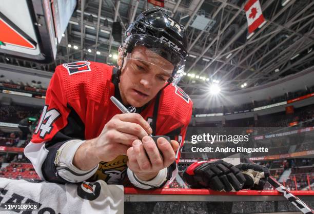 Mark Borowiecki of the Ottawa Senators autographs a puck for a young fan during warmup prior to a game against the Colorado Avalanche at Canadian...