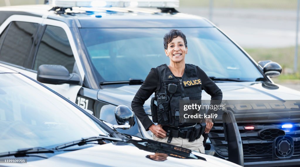 Mujer policía afroamericana de pie junto a un coche patrulla