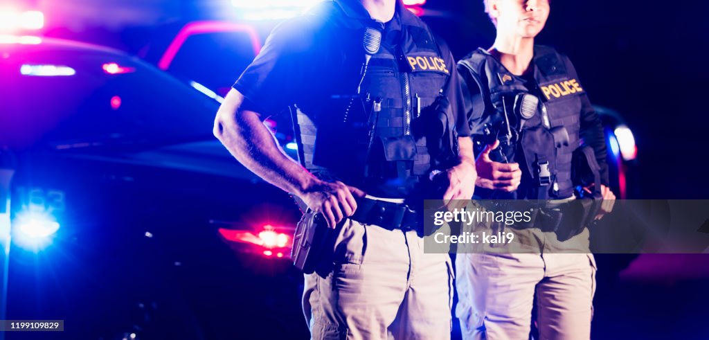 Two police officers standing in front of patrol cars