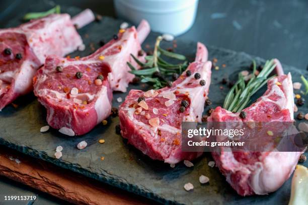 raw lamb chops prepared on a dark slate cutting board with a ramekin or pesto on the side with rosemary and other herbs - raw food stock pictures, royalty-free photos & images