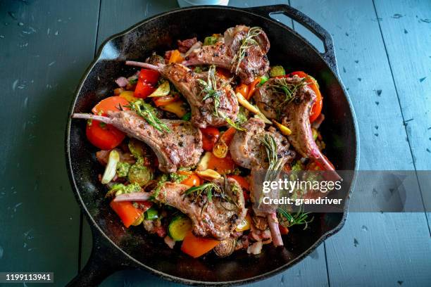 gusseisen skillet gefüllt mit gourmet lamm koteletts und ein gemüse medley von rosenkohl, paprika, knoblauch, lauch tomaten, knoblauch und pesto - lammbraten stock-fotos und bilder