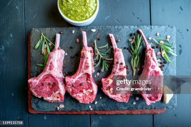 raw lamb chops prepared on a dark slate cutting board with a ramekin or pesto on the side with rosemary and other herbs - lamb chop stock pictures, royalty-free photos & images