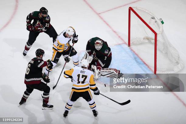 Goaltender Adin Hill of the Arizona Coyotes makes a save as Patric Hornqvist and Bryan Rust of the Pittsburgh Penguins look for a rebound during the...