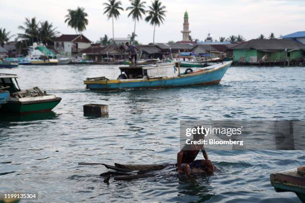 Youth floats on piece of wood off Manggar Village Pier in the port city of Balikpapan in East Kalimantan, Borneo, Indonesia, on Tuesday, Nov. 26,...