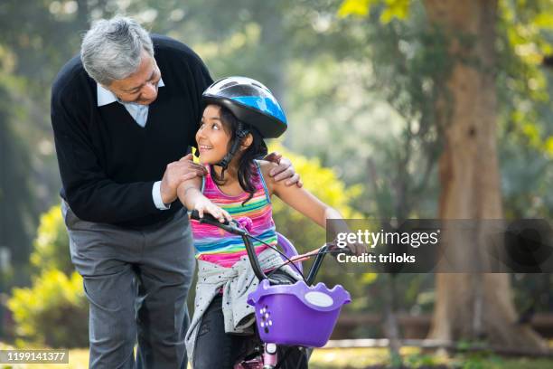 grandfather teaching her granddaughter cycling at park - indian riding stock pictures, royalty-free photos & images