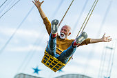 Carefree mature man having fun on chain swing ride in amusement park.