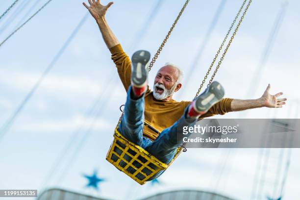 carefree mature man having fun on chain swing ride in amusement park. - freedom stock pictures, royalty-free photos & images