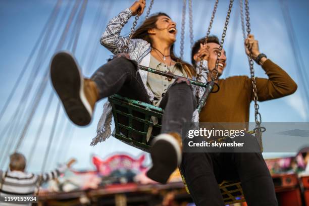 young carefree couple on chain swing ride at amusement park. - carousel swings stock pictures, royalty-free photos & images