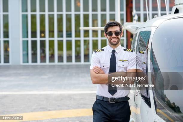 helicopter pilot in uniform standing arms cross near helicopter on a landing point. - helicopter pilot stock pictures, royalty-free photos & images