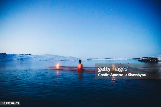 vrouw met bad in thermaal zwembad met uitzicht op de besneeuwde bergen en bevroren meer in ijsland - winter swimming pool stockfoto's en -beelden