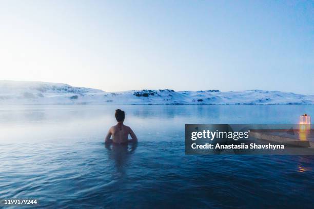 woman having bath in thermal pool with view of the snowy mountains and frozen lake in iceland - red tub stock pictures, royalty-free photos & images