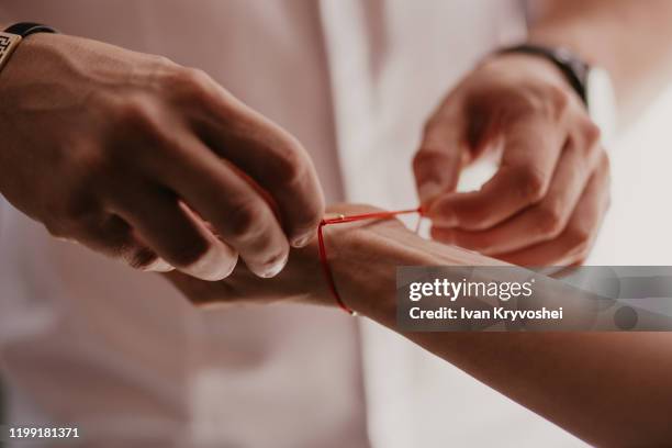 man ties a red bracelet on woman's hand, red thread, jewelry, bracelet with a stone, women's accessories. authentic love - pulseira - fotografias e filmes do acervo