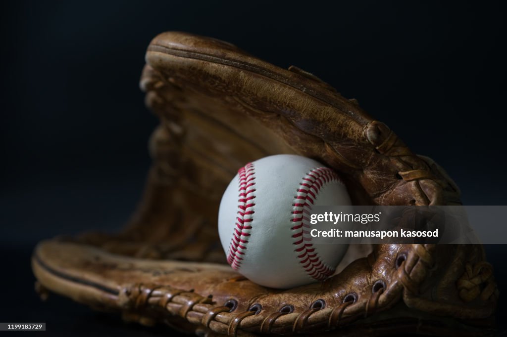 Baseball in a glove on black background.