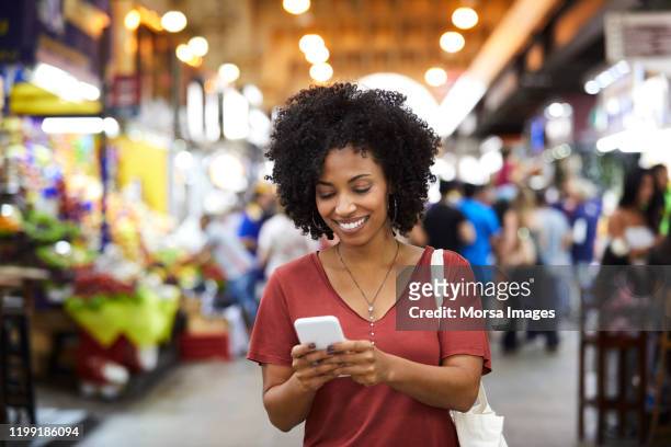 donna sorridente che usa lo smartphone al supermercato - consumerism foto e immagini stock