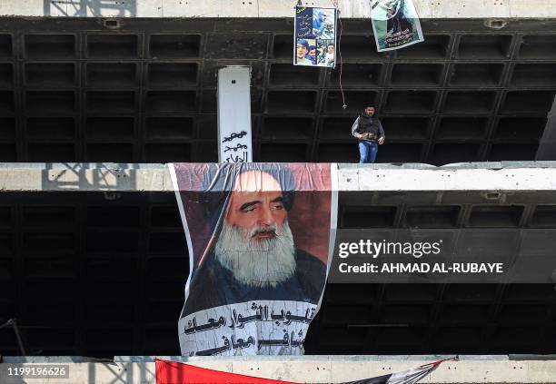 Protester stands above a poster of Grand Ayatollah Ali Sistani, Iraq's top Shiite cleric, hanging from the "Turkish Restaurant" high-rise building...